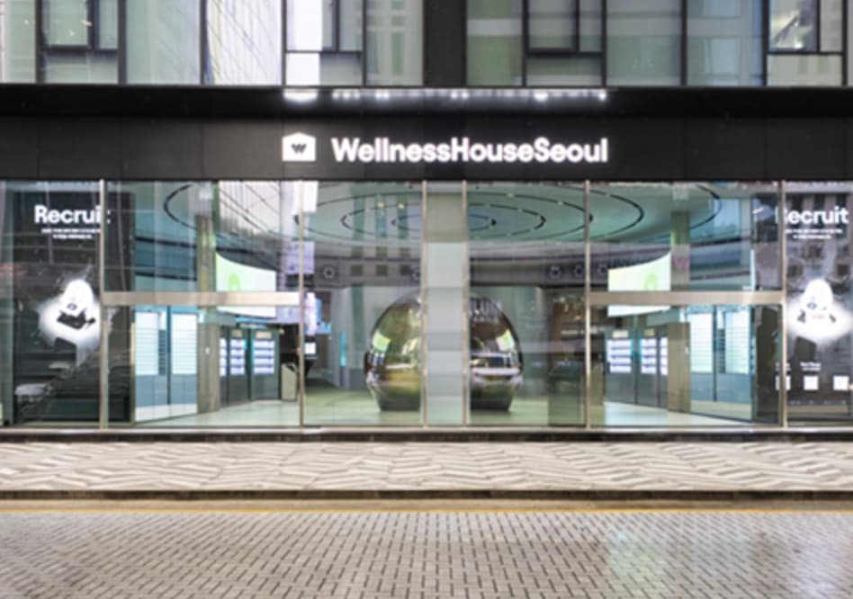 Glass storefront of Wellness House Seoul at night with its logo sign lit above the entrance